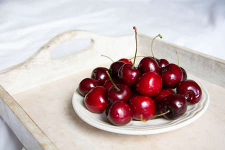 A ripe cherry in a saucer is on a wooden tray on a light background. Fresh and beautiful cherry berries are on a plate.の写真素材