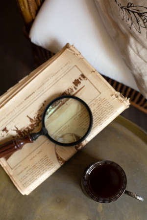Glass of tea in an iron cup holder, a newspaper and a magnifying glass are on the table against the background of the interior in retro style. View from the top point. A vertical image.の写真素材
