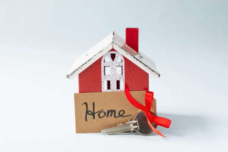 Key to the apartment with a tag with the inscription - home and the red decorative house are on a blue background. The topic of buying or purchasing an apartment.の写真素材