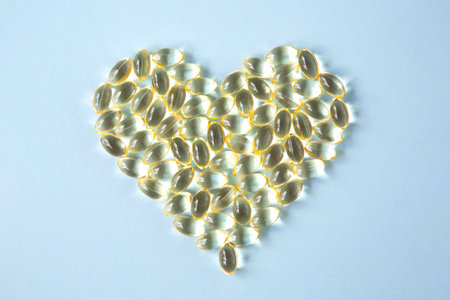 Transparent capsules with vitamin D or Omega-3 in the form of a heart is on a blue background. view...