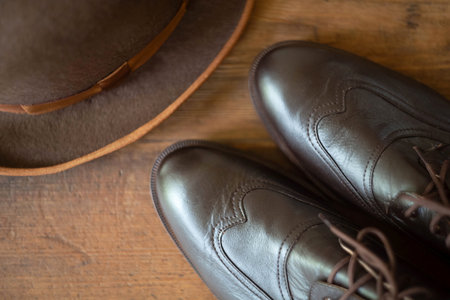 Fragment of men's brown boots blind brogues and bowler hat on a wooden background. Vintage men's English style. view from the top.の写真素材