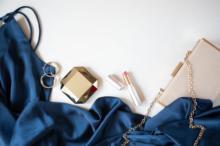 Women's gold-colored accessories, handbag and cocktail dress in blue are on a light background....