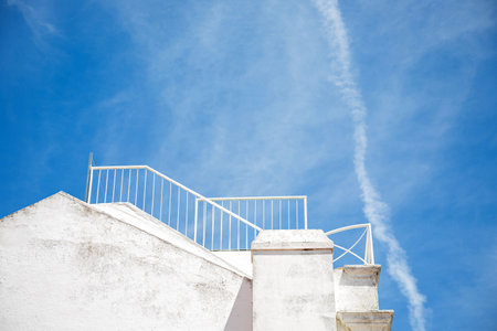 Part of the roof of a traditional whitewashed house with a staircase against a blue sky....