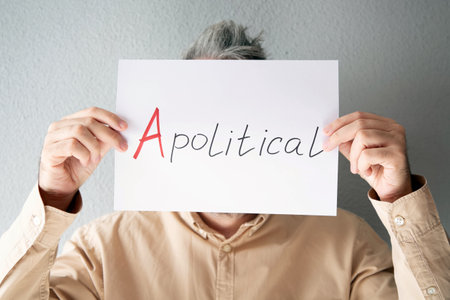 A man in a beige shirt holds a sheet of paper in front of his face with an inscription - Apolitical.の写真素材