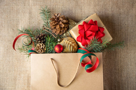 A paper bag with a gift with a red bow, spruce spruce twigs and Christmas toys on a burlap...