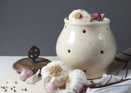A ceramic garlic jar with a wooden lid and the garlic heads are on the table.の写真素材