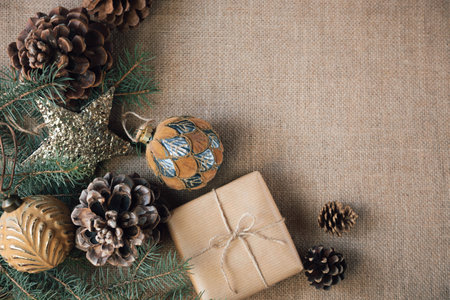 A gift wrapped in paper is placed on a burlap background, surrounded by Christmas beautiful decorations. Copy space. Vintage style.の写真素材