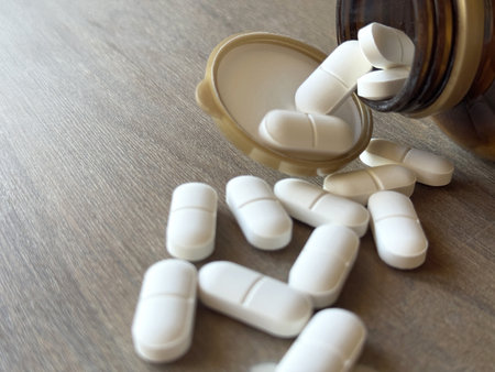 Pills spilling out of pill bottle on wooden background. Focus on foreground, soft bokeh.の写真素材