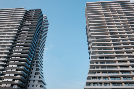 Modern high-rise apartment buildings with repeating balconies against blue sky, showcasing...