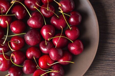Red cherries on a brown plate on a wooden table. Summer food, healthy eating. Organic, vegetarian, vegan, dietary, diabeticの写真素材