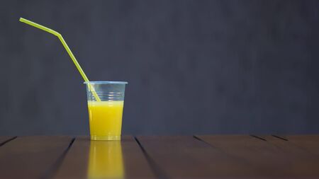 Orange juice in a plastic Cup with a tube on a brown background. Copy space. Picnic, vegan, healthy...