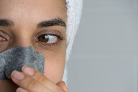 A woman sticks a cleansing strip on her nose. Black dots on the nose. Girl without makeup in the bathroom. Skin care, problem skin, cleansing. Natural beauty, naturalness. Blackheads and comedones.の写真素材