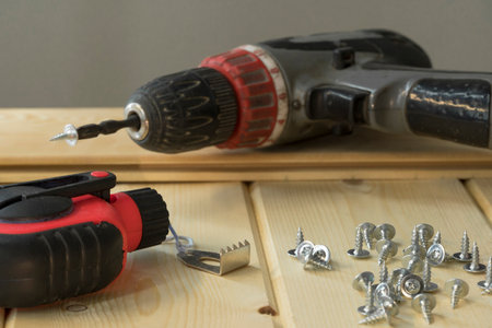 Cordless drill and screws. Electric drill with drill bits, screws on wooden background. Bunch of screws on wood planks. Assorted tools. Handyman professional DIY project workplace tabletop.の写真素材