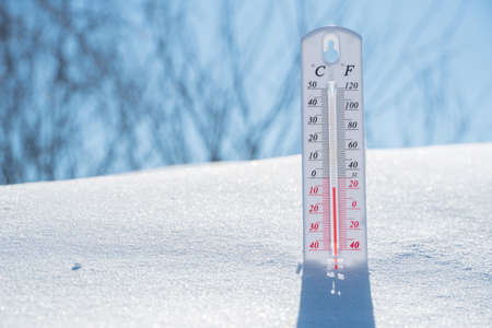 The thermometer lies on the snow and shows a negative temperature in cold weather on the blue...