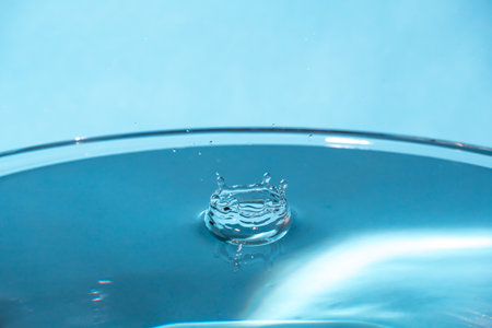 Water splash in crown shape and falling drop. Splash of the falling drops of water. Water drop on blue background. Blue water surface with splash. Clear Waterdrop with circular waves. Splashes closeupの写真素材