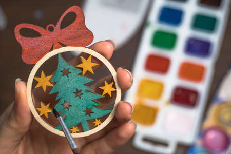 Paint the Christmas tree toy with colors. Create a decoration for the new year at home. Hobbies and creativity, handmade. The artist draws on a wooden toy. Art, creation. Decorate the christmas ballの写真素材