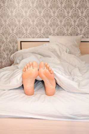 Womans feet under the blanket in the morningの写真素材