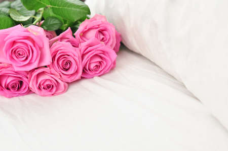 Bouquet of pink roses on the white linens on bedの写真素材