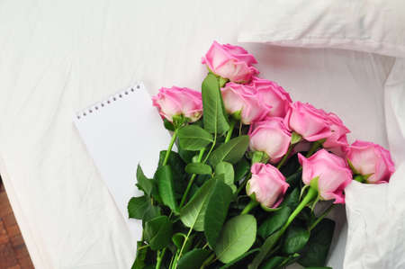 Bouquet of pink roses on the white linens on bedの写真素材