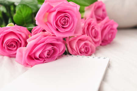 Bouquet of pink roses on the white linens on bedの写真素材