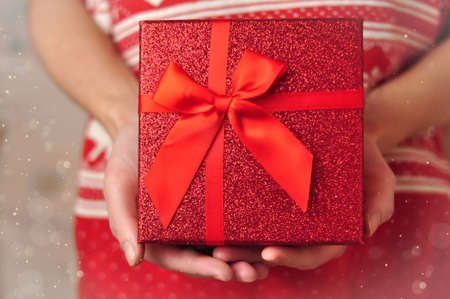 Present red box with bow in hands giving giftsの写真素材