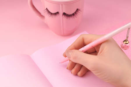 Hand holding pen and make notes in pink notebook . High quality photoの写真素材