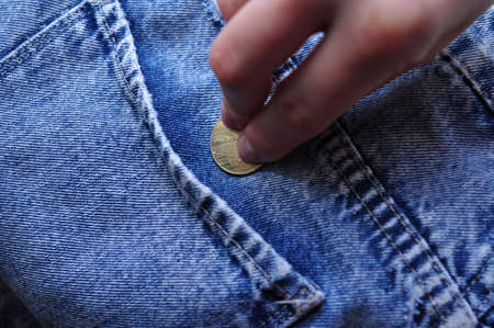 hand puts gold coin change in jeans pocket .Savings concept