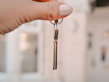 Womans hand with metal keys on blurred background with house. High quality photoの写真素材
