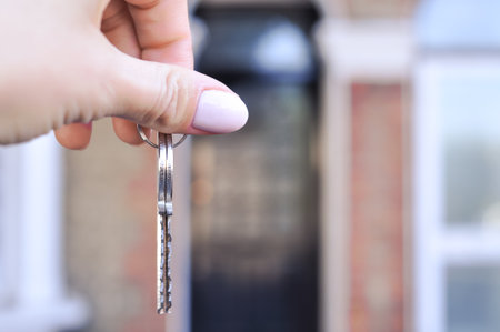Womans hand with metal keys on blurred background with house. High quality photoの写真素材