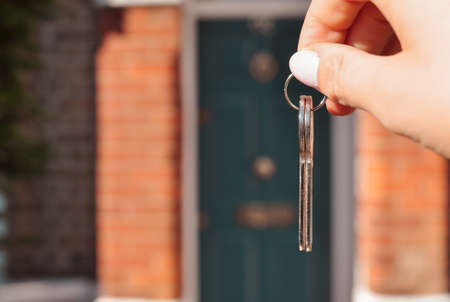 Womans hand with metal keys on blurred background with house. High quality photo