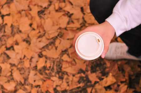 Paper glass of coffee in hand on the orange autumn leaves background . High quality photoの写真素材