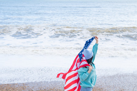 brunette woman in blue sweater and hat with american national flag near sea on the coastlineの写真素材