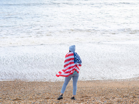 brunette woman in blue sweater and hat with american national flag near sea on the coastlineの写真素材
