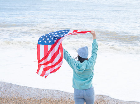 brunette woman in blue sweater and hat with american national flag near sea on the coastlineの写真素材