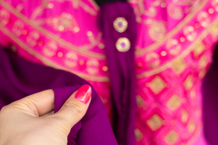 woman's hand holding indian colorful pink and purple dress with golden pattern.の写真素材