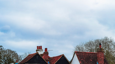 A cloudy blue sky over a small house rooftop with a chimney in an English townの写真素材