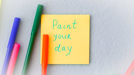 Inspirational phrase on a colorful sticky note, reminding to color your day brightの写真素材