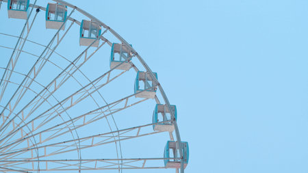 Ferris wheel closeup with metal frame and cabins over bright blue sky.の写真素材