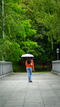 A woman with an umbrella walking alone on a quiet park path in spring nature...の写真素材