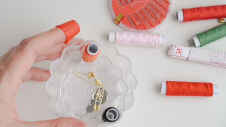 Sewing composition with threads, pins, and tape on neutral white surface.の写真素材