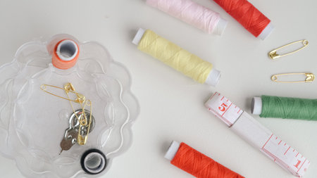Sewing composition with threads, pins, and tape on neutral white surface.の写真素材