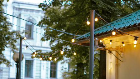 Warm glowing garland lights decorating outdoor seating area in city cafe.の写真素材