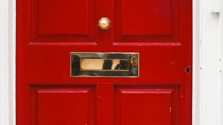 Architectural fragment of English home red door with vintage mail slot and handle.