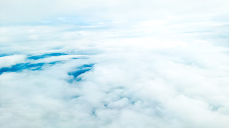 View through plane window showing high altitude clouds and endless blue sky.