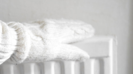 Warm hand touching a white radiator, illustrating home heating and cozy winter comfort.の写真素材