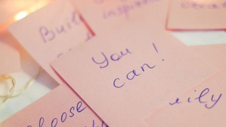 Close-up of pink sticky notes with motivational phrases written in blue ink on a table