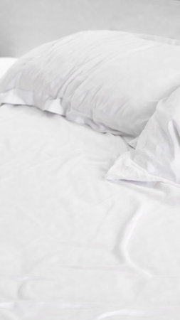 Soft white bedding and two pillows arranged on a bed in a bright, minimalistic room