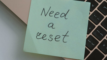 Green sticky note on a laptop keyboard with handwritten text indicating a need for a reset