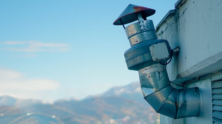 Metal ventilation pipe with a conical cap mounted on a rooftop against a mountain landscape