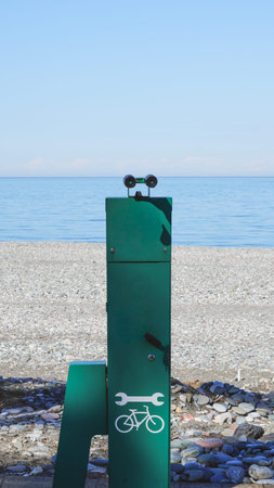 Green bicycle repair station with tool symbol near pebbled beach and calm ocean water